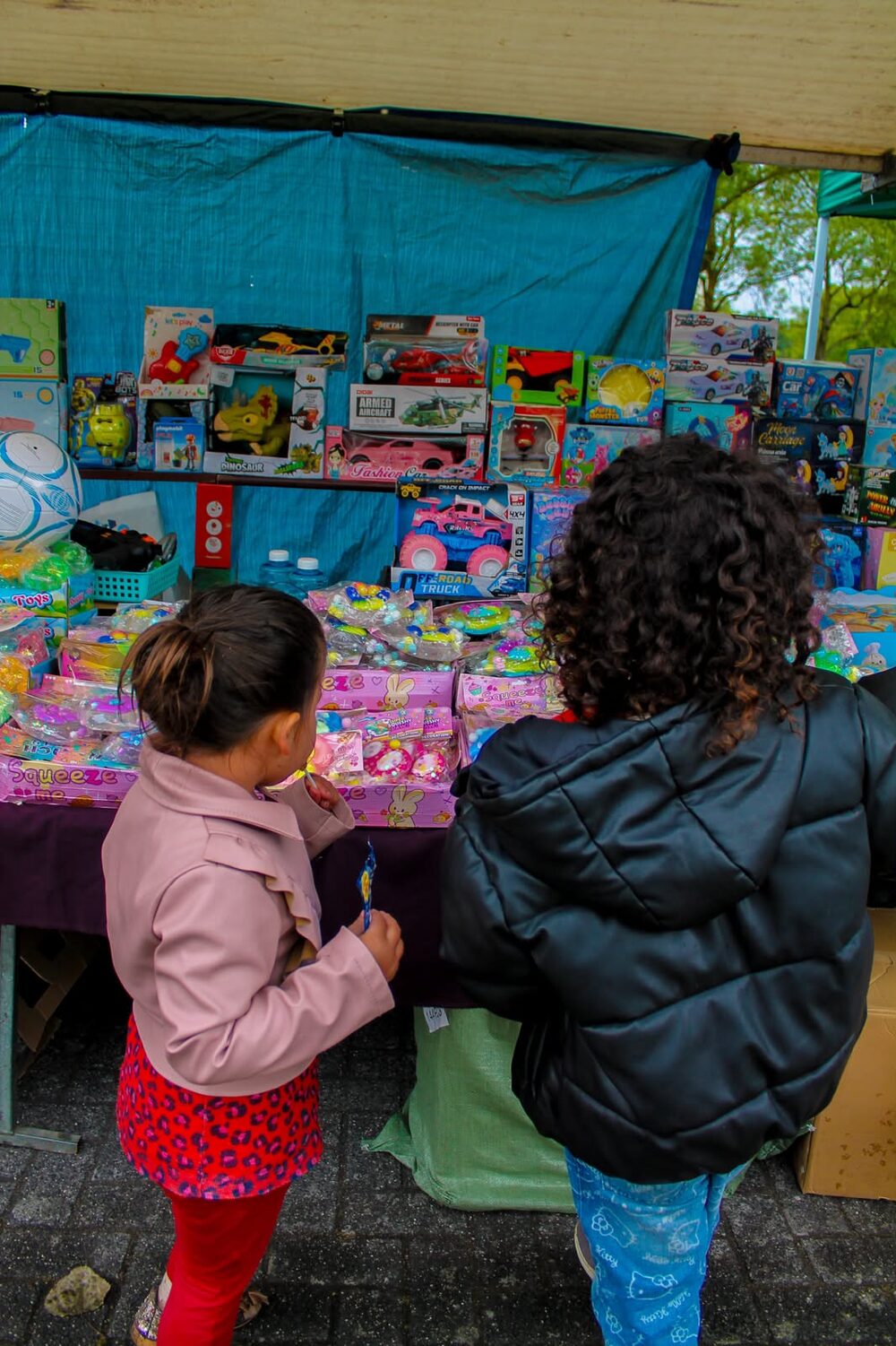 Twee kinderen, op de rug gezien, bekijken de speelgoedkraam op de kermes