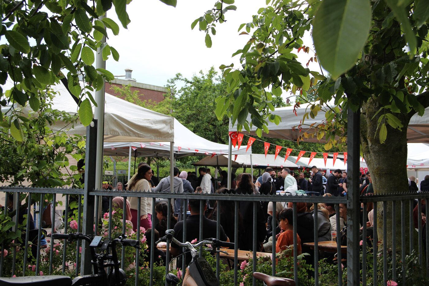 Een vol plein met tenten, vlaggetjes en bezoekers tijdens de kermes, gezien door de bomen